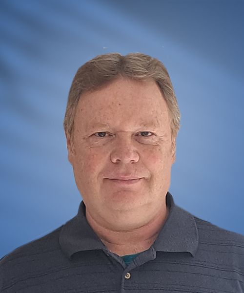 Man with short brown hair smiles, wearing a dark blue polo shirt. Blue background.