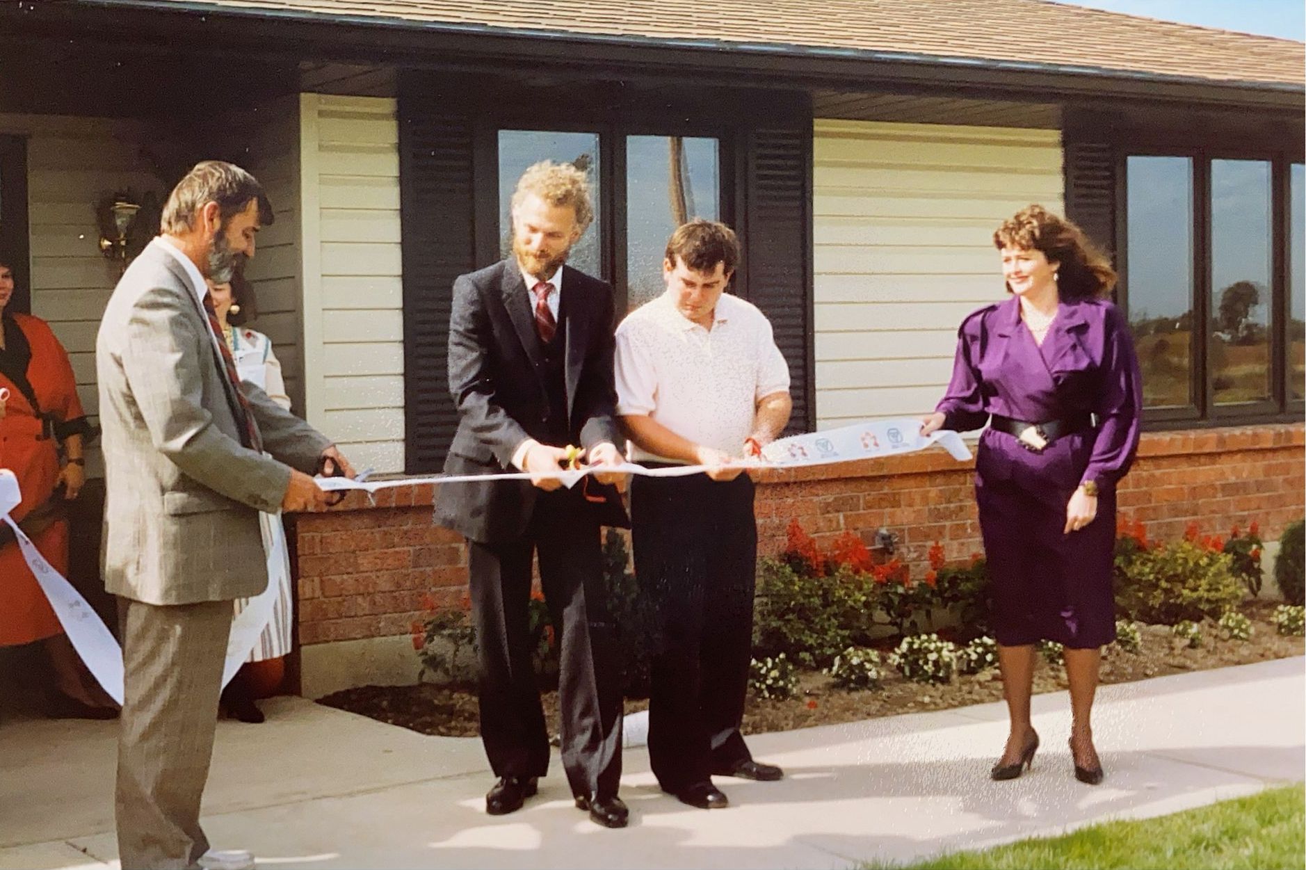 People cutting a ribbon in front of a building; a ribbon-cutting ceremony.
