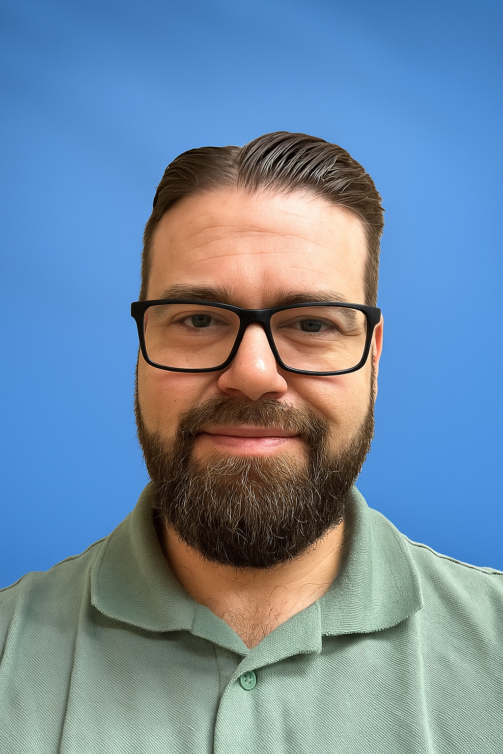Man with beard and glasses smiling, wearing a light green polo against a blue background.