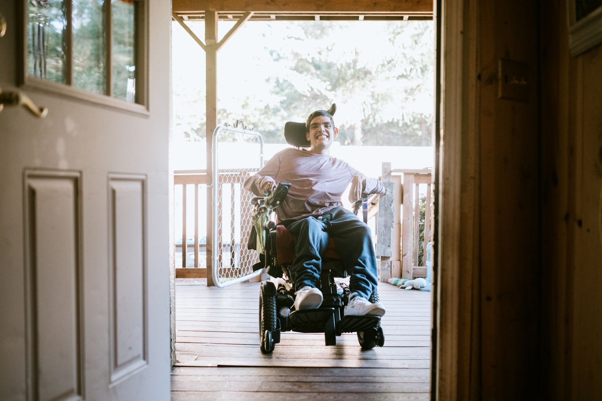 Person in wheelchair on a porch, smiling, looking at the camera.