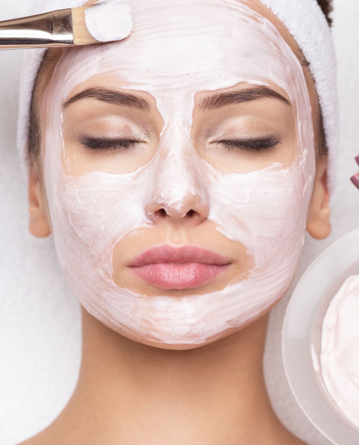 A woman is getting a facial treatment with a brush on her face.