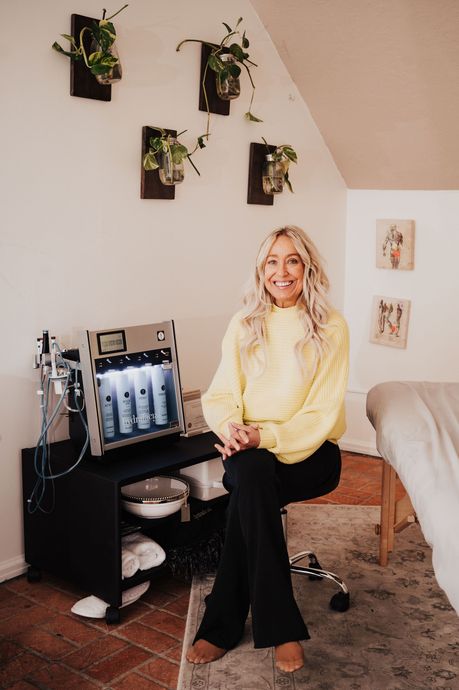 A woman in a yellow sweater is sitting on a stool in front of a machine.