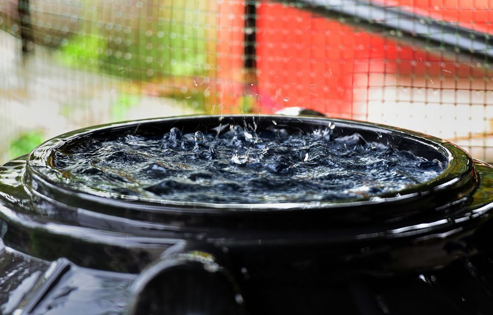Rain Is Falling On A Black Barrel Filled With Water — Clear and Clean Water Tank Cleaning Services in Murrurundi, NSW