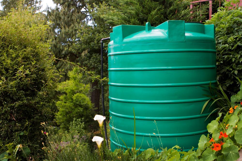 A Green Water Tank Is Sitting In The Middle Of A Garden — Clear and Clean Water Tank Cleaning Services in Murrurundi, NSW