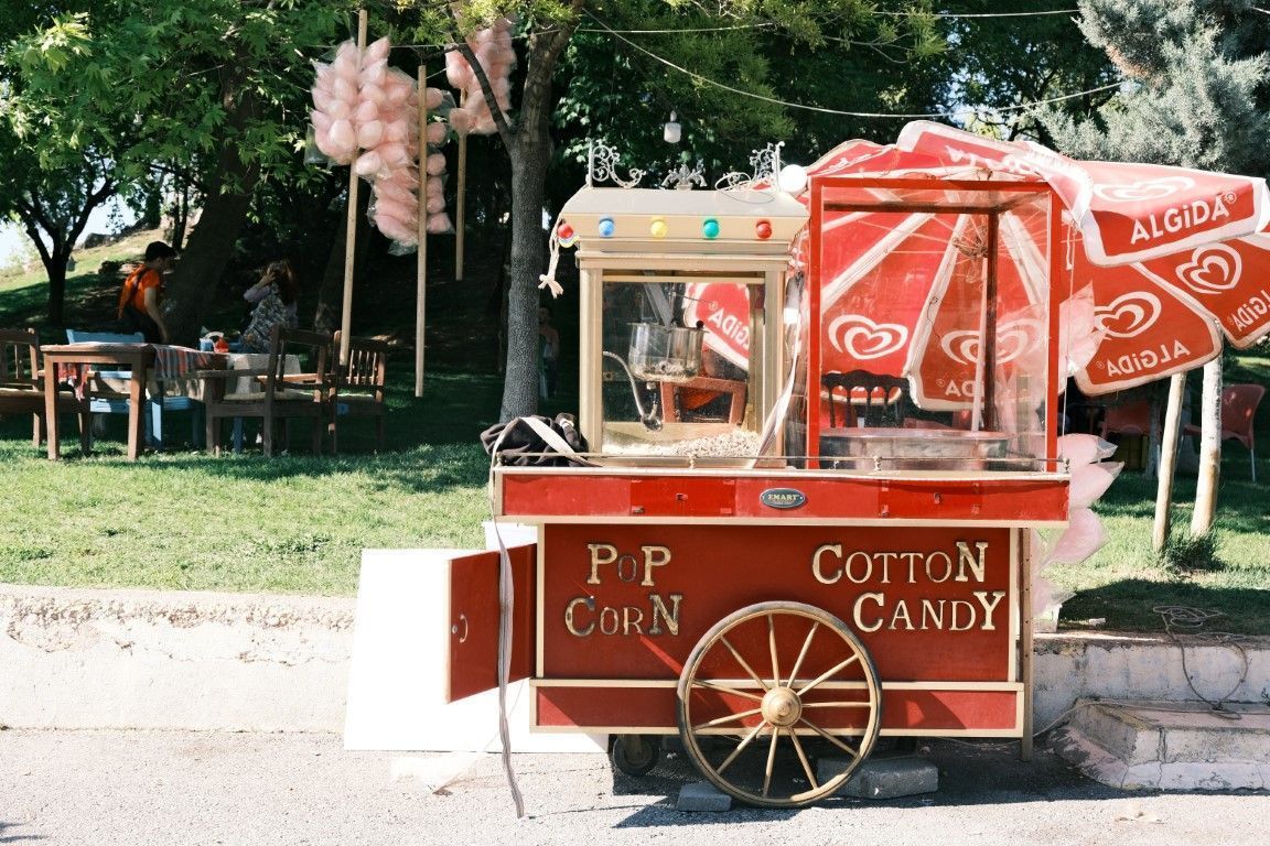 Red cotton candy cart in a park with a Coca-Cola umbrella and a small snack stand