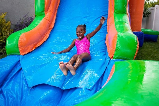Child in pink swimsuit sliding down a colorful inflatable water slide, smiling with arms outstretched