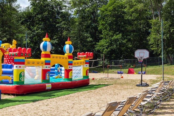 Colorful inflatable bounce house and slide set on a grassy park area with chairs and a basketball hoop nearby
