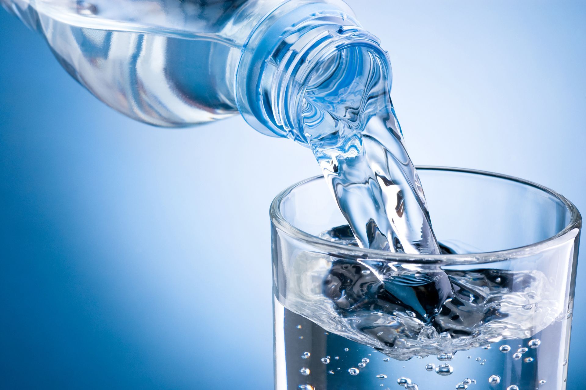 Clear water pouring from a bottle into a glass against a blue background