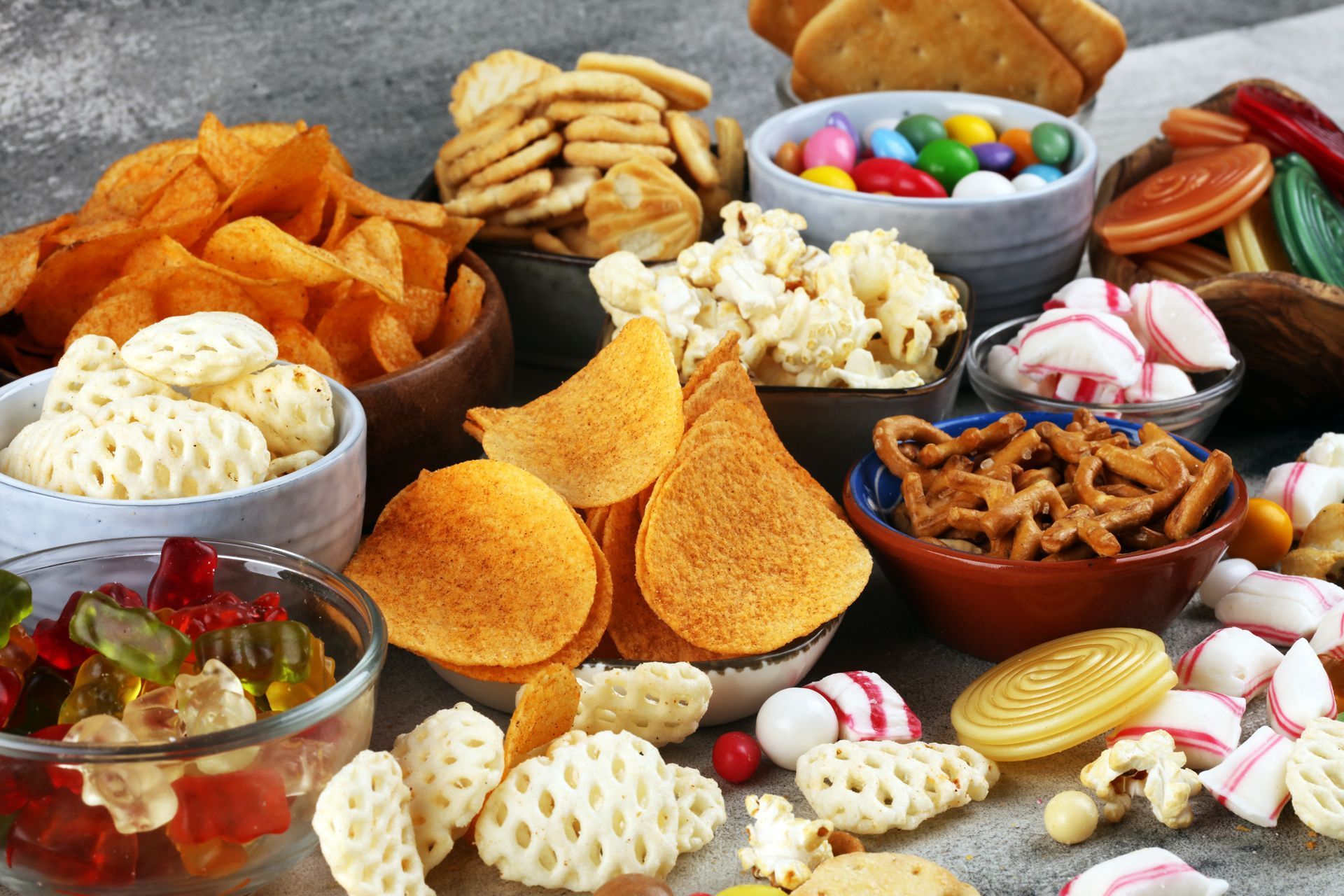 Assorted colorful snacks and chips arranged in bowls on a white background