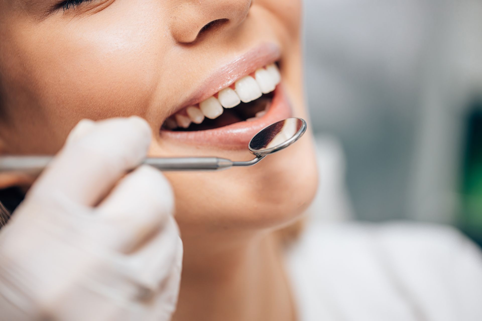 Dentist examining a smiling patient’s teeth with a dental mirror and gloved hand