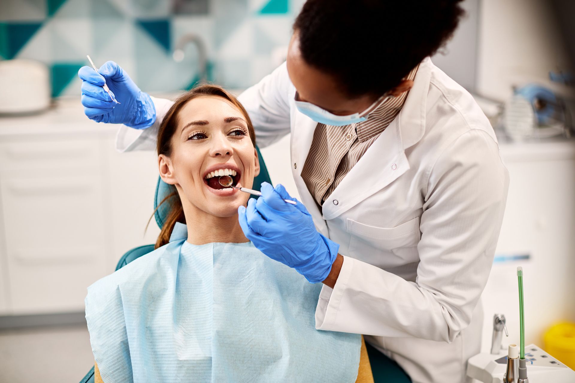 Dentist examining a smiling patient in a dental chair, wearing blue gloves and a white coat.