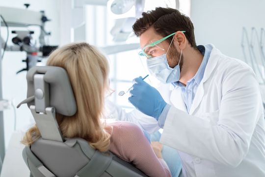 Dentist examining a patient in a bright dental clinic while wearing a mask and gloves