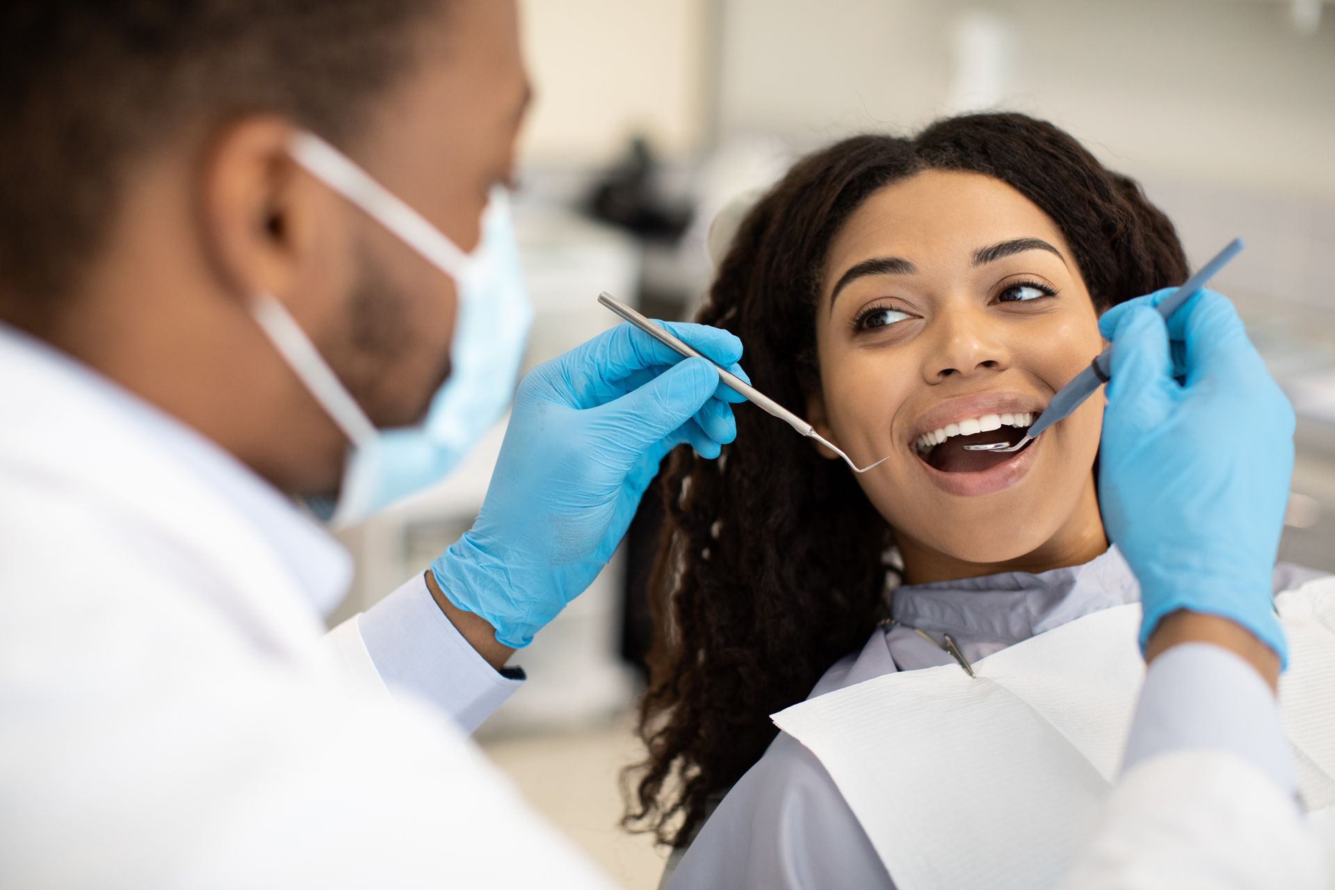 Dentist examining a smiling patient with tools, wearing blue gloves in a clinic setting
