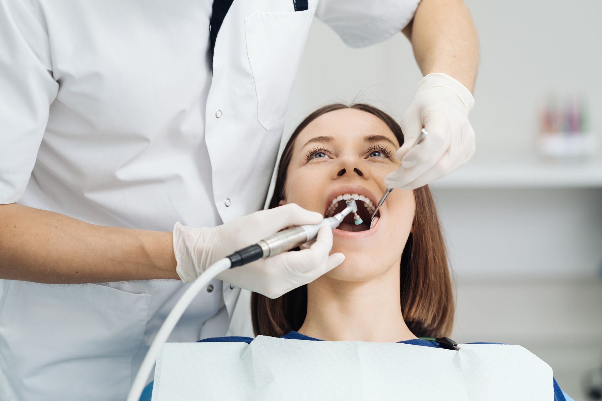 Dentist using tools to examine a patient’s open mouth in a bright clinic