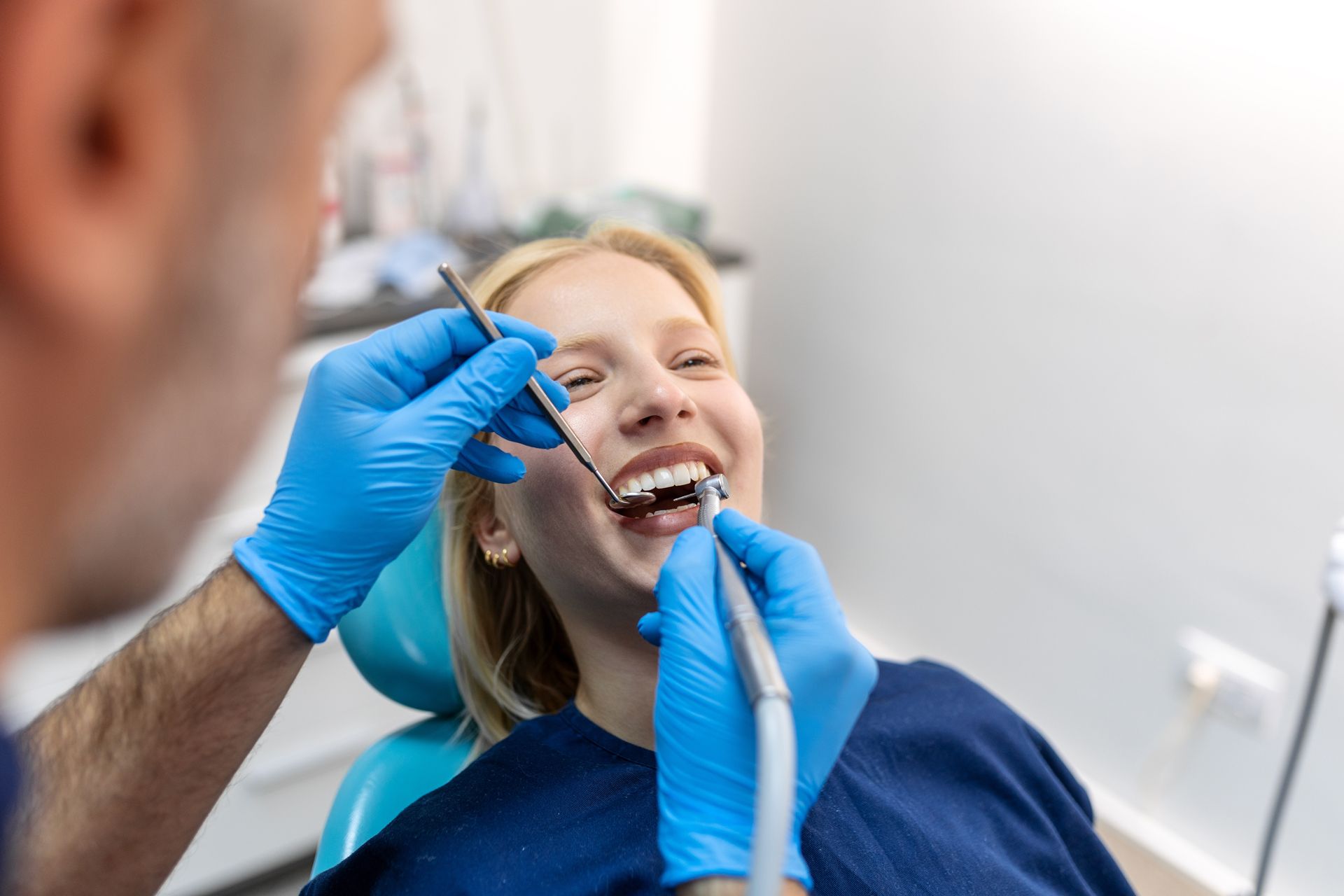 Dentist examining a smiling patient’s teeth with blue gloves and dental tools