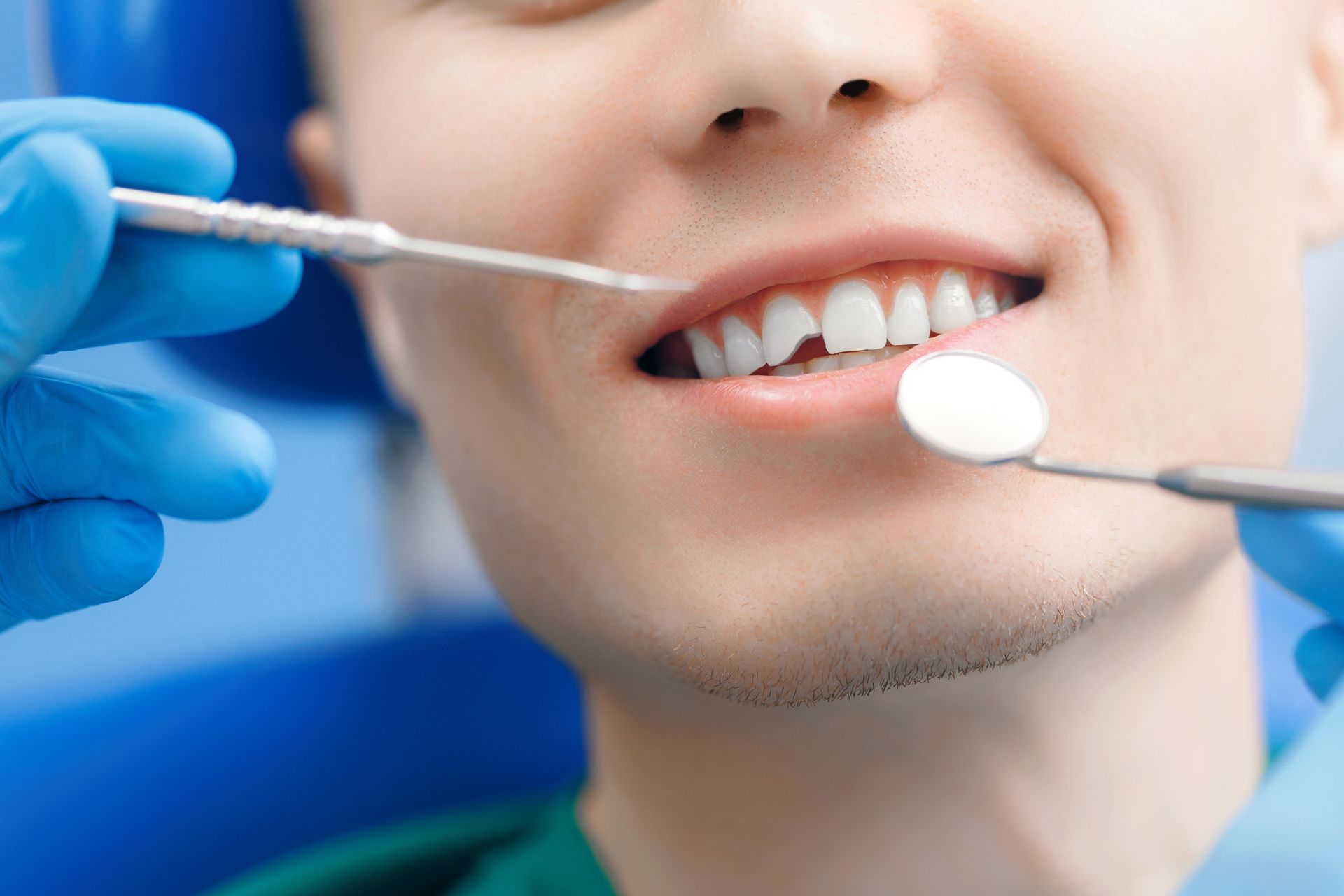 Dentist examining a smiling patient’s teeth with dental tools and mirror