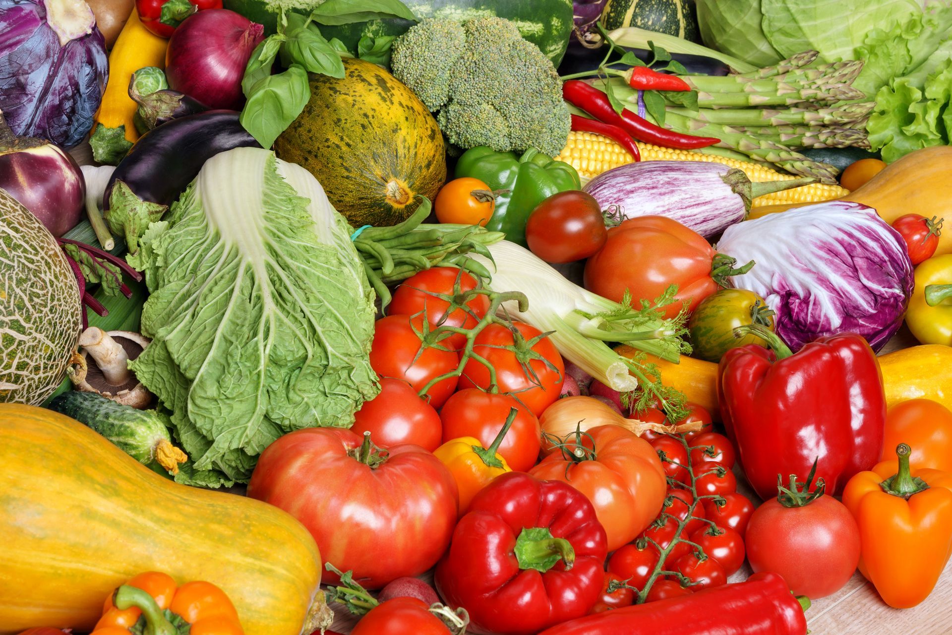 Assorted colorful fresh vegetables piled together, including tomatoes, peppers, cabbage, eggplant, and squash.
