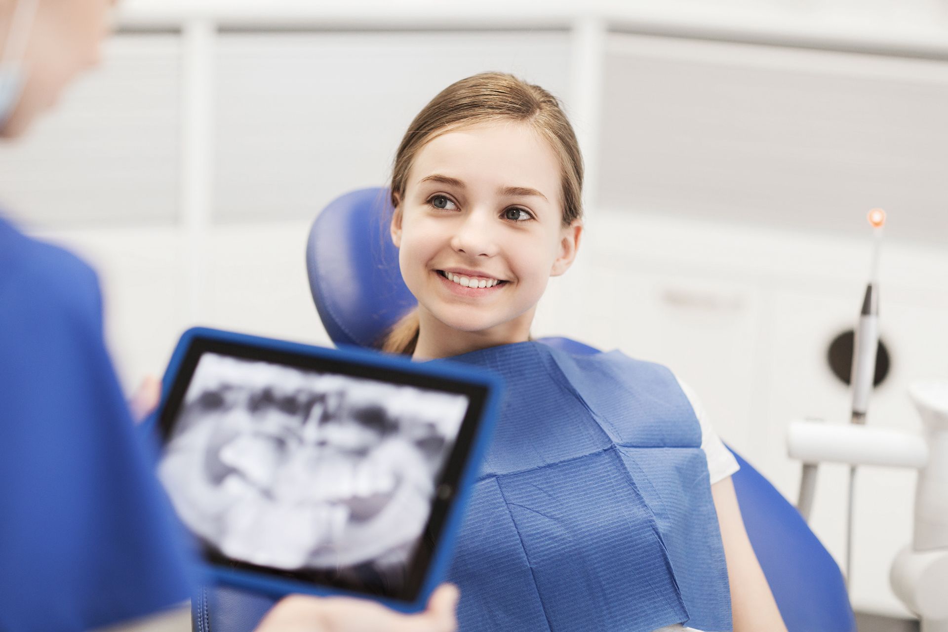 Smiling dental patient in blue bib, with dentist holding an X-ray viewer in a bright clinic
