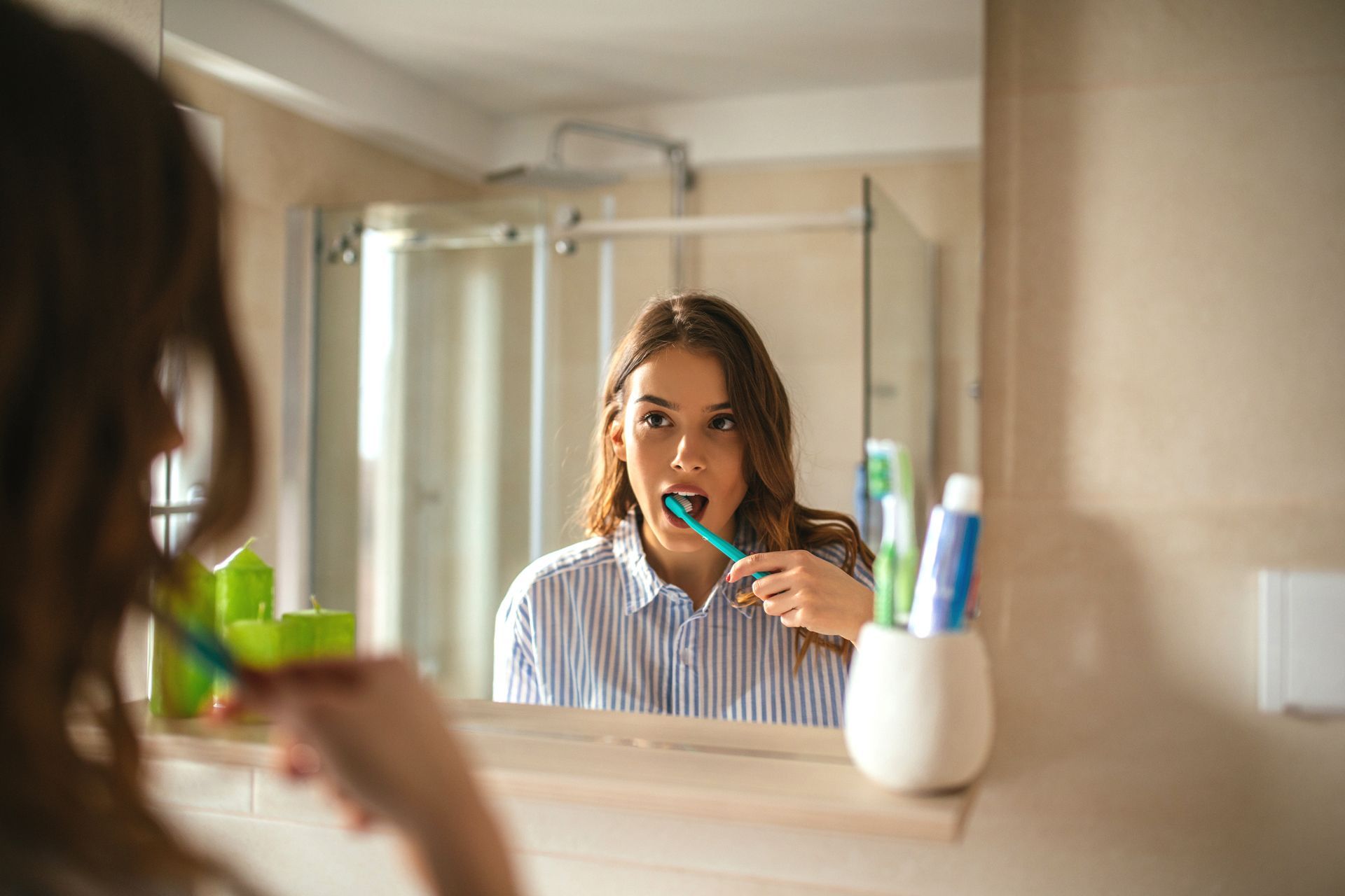 Woman brushing teeth in a bathroom mirror, with a toothbrush holder on the sink.
