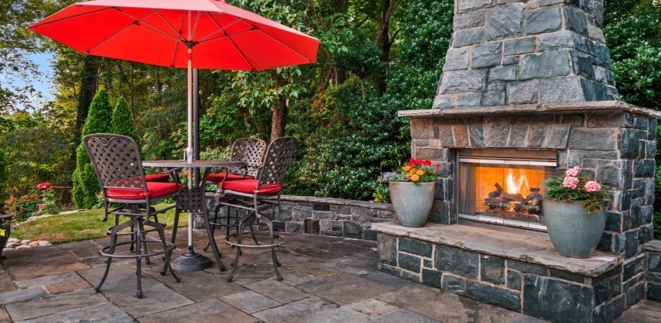 Outdoor patio with a stone fireplace, table, chairs, and red umbrella.