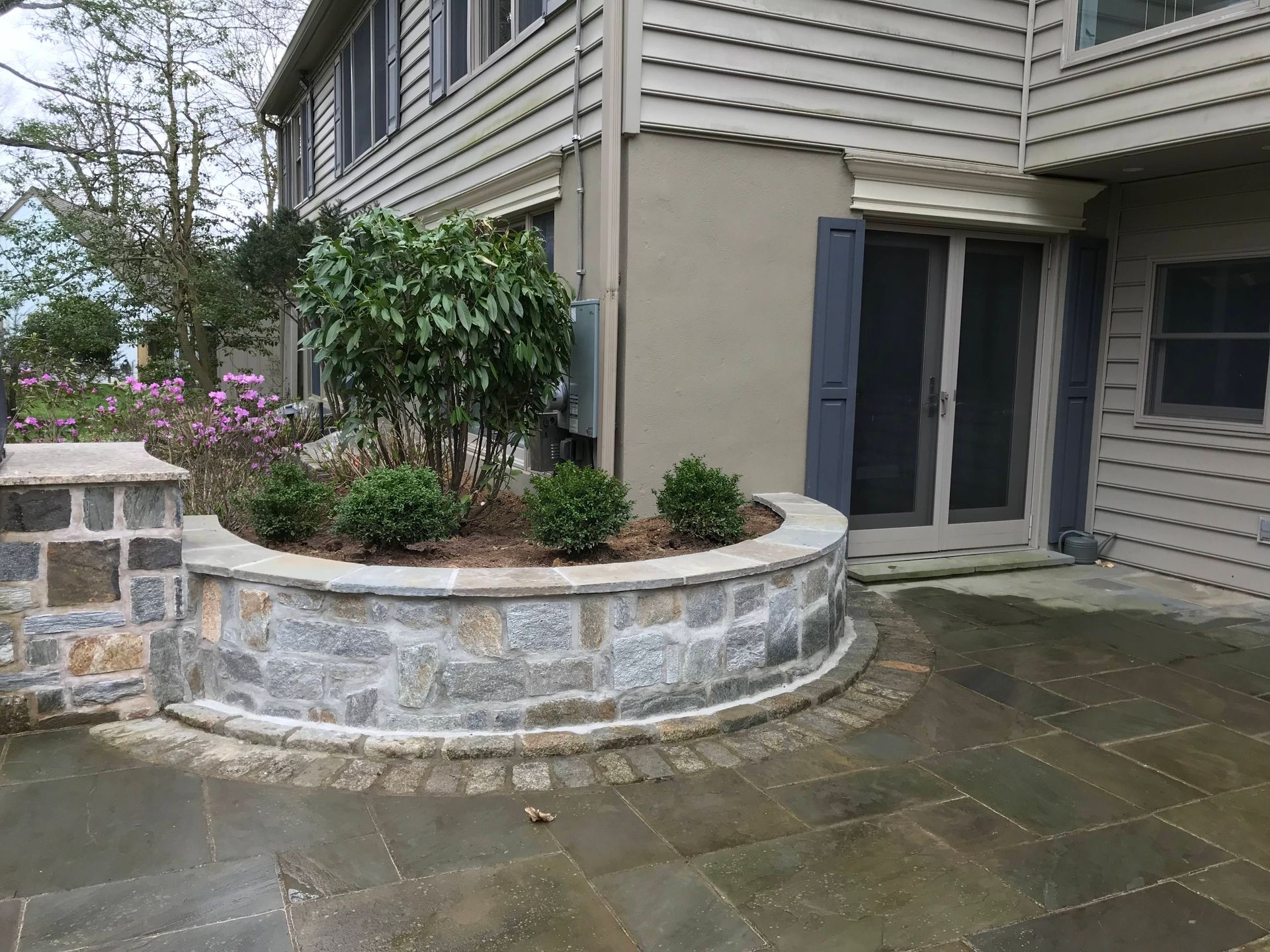 Patio with stone pavers, a fountain, and lush greenery. Sunny day.