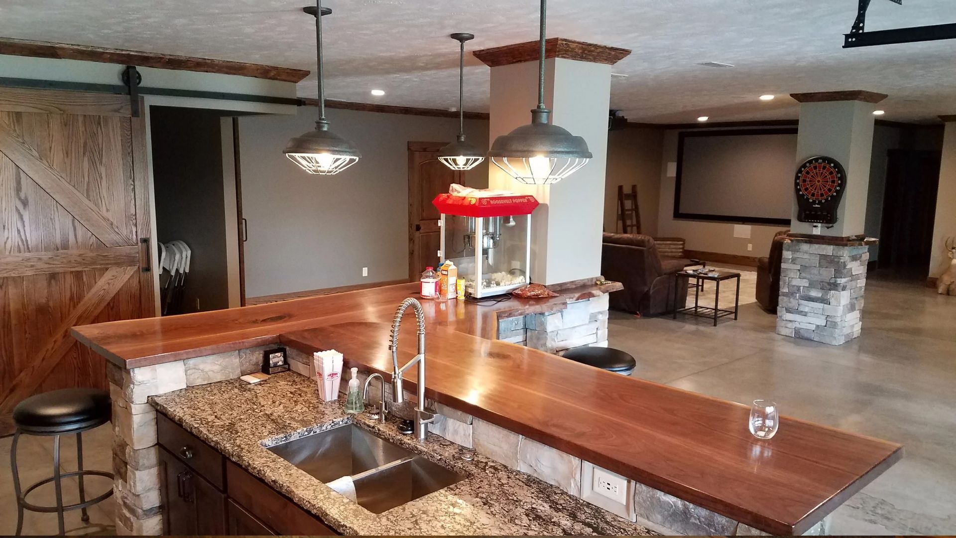 Bar with wood countertops, stone accents, pendant lights, and popcorn machine. Sliding barn door