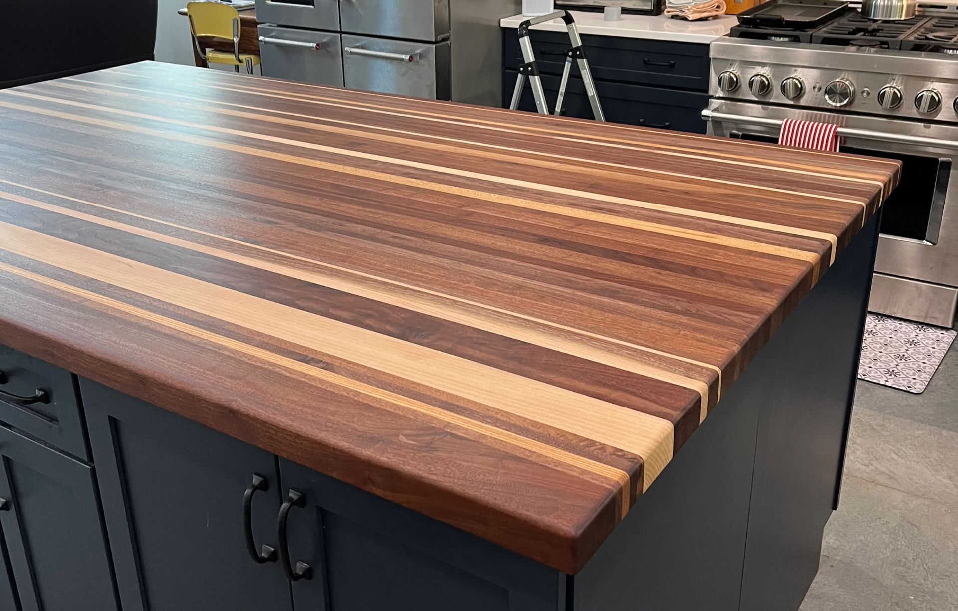 Butcher block island countertop with dark and light wood strips in a kitchen.