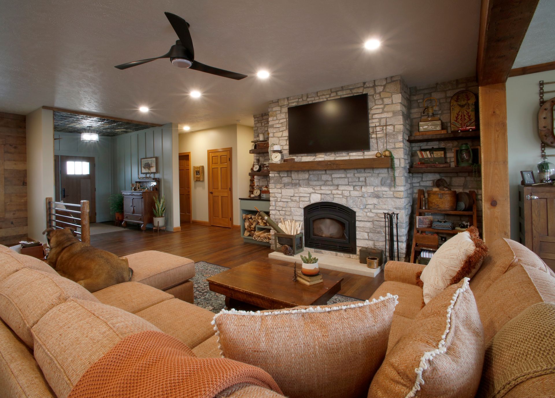 Fireplace with light stone facing, TV, black shelves with decorations, and wood flooring.