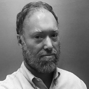 Man with beard in striped shirt looking at camera.