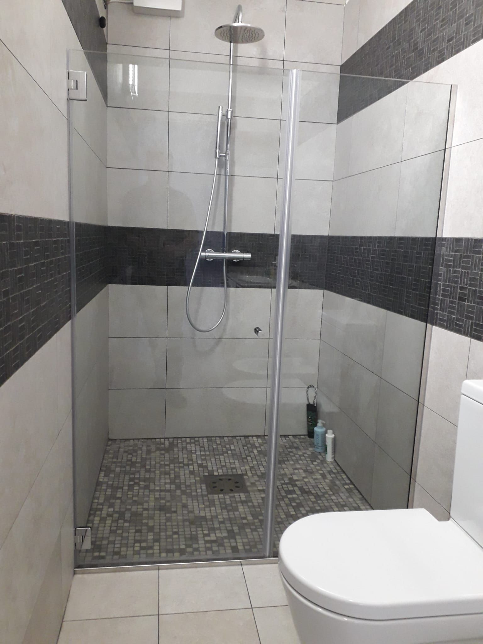 Bagno moderno piastrellato con box doccia in vetro, soffione a pioggia e WC in primo piano.