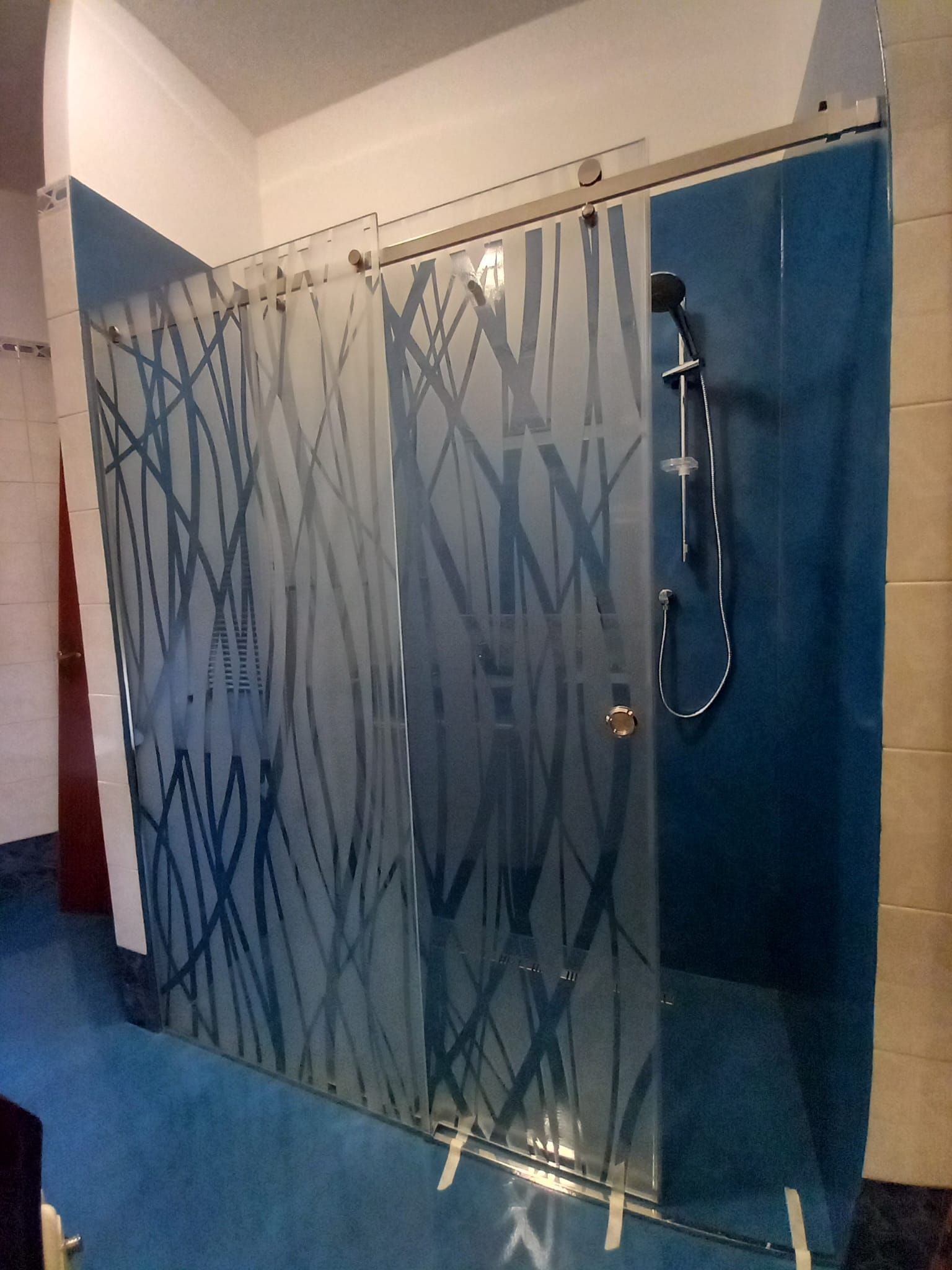 Box doccia moderno in vetro con motivo a foglie blu satinate e soffione a parete.
