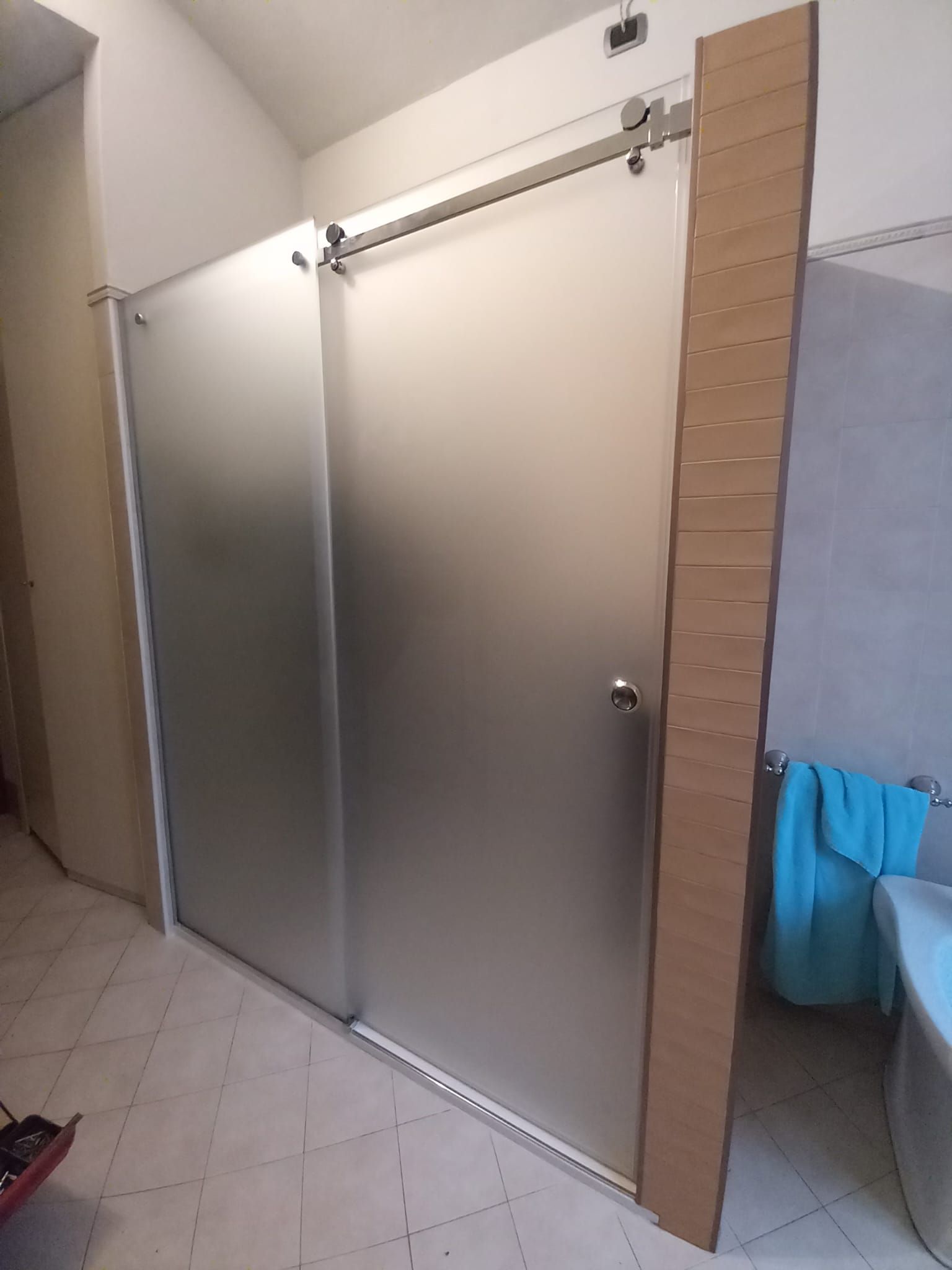 Porte in acciaio inossidabile in un box doccia piastrellato, con un asciugamano blu appeso sulla destra.