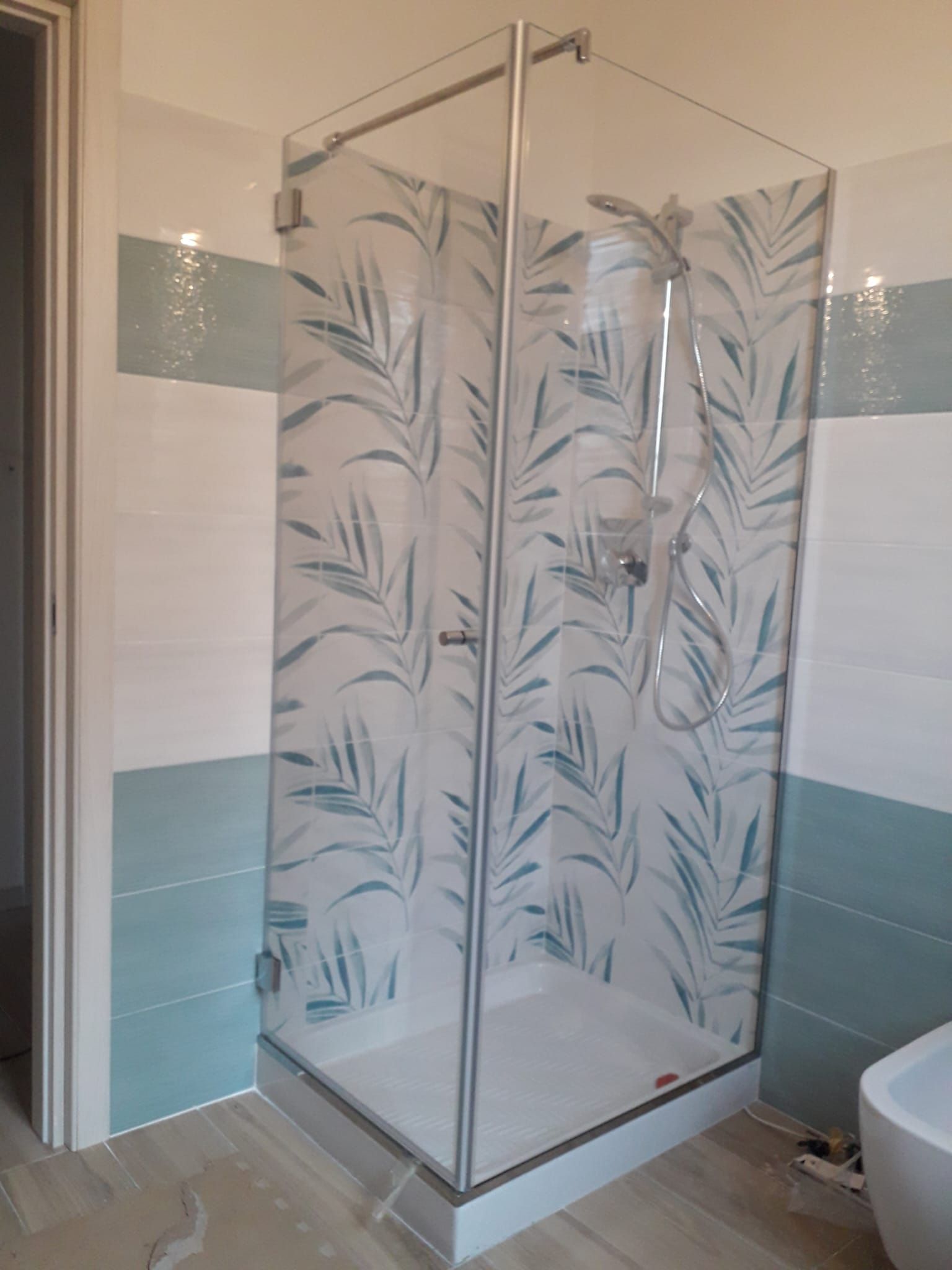 Box doccia angolare con pannelli in vetro satinato a motivo fogliare in un bagno piastrellato.