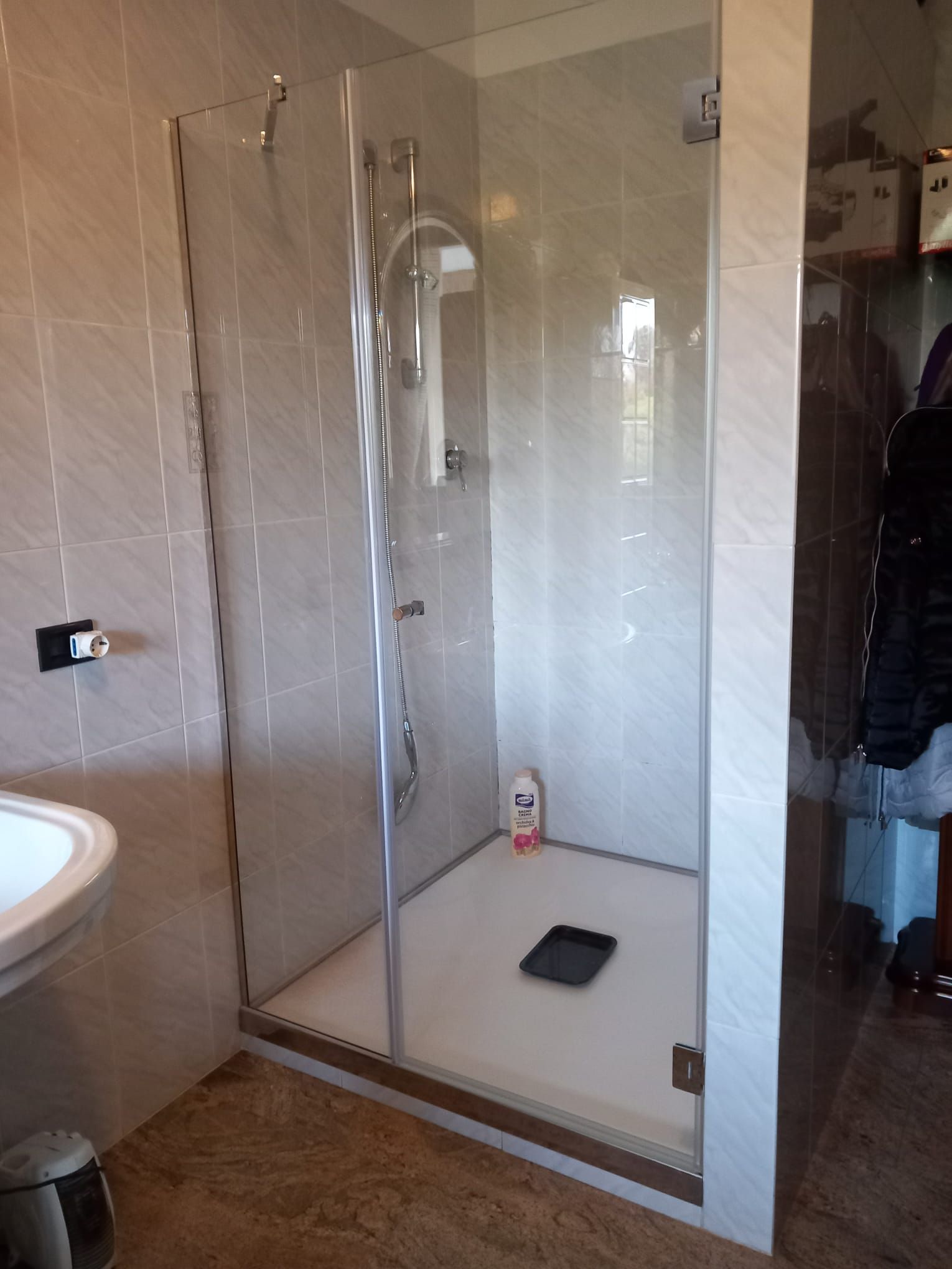 Bagno moderno con box doccia in vetro, rubinetteria cromata, piastrelle beige e lavabo a parete.