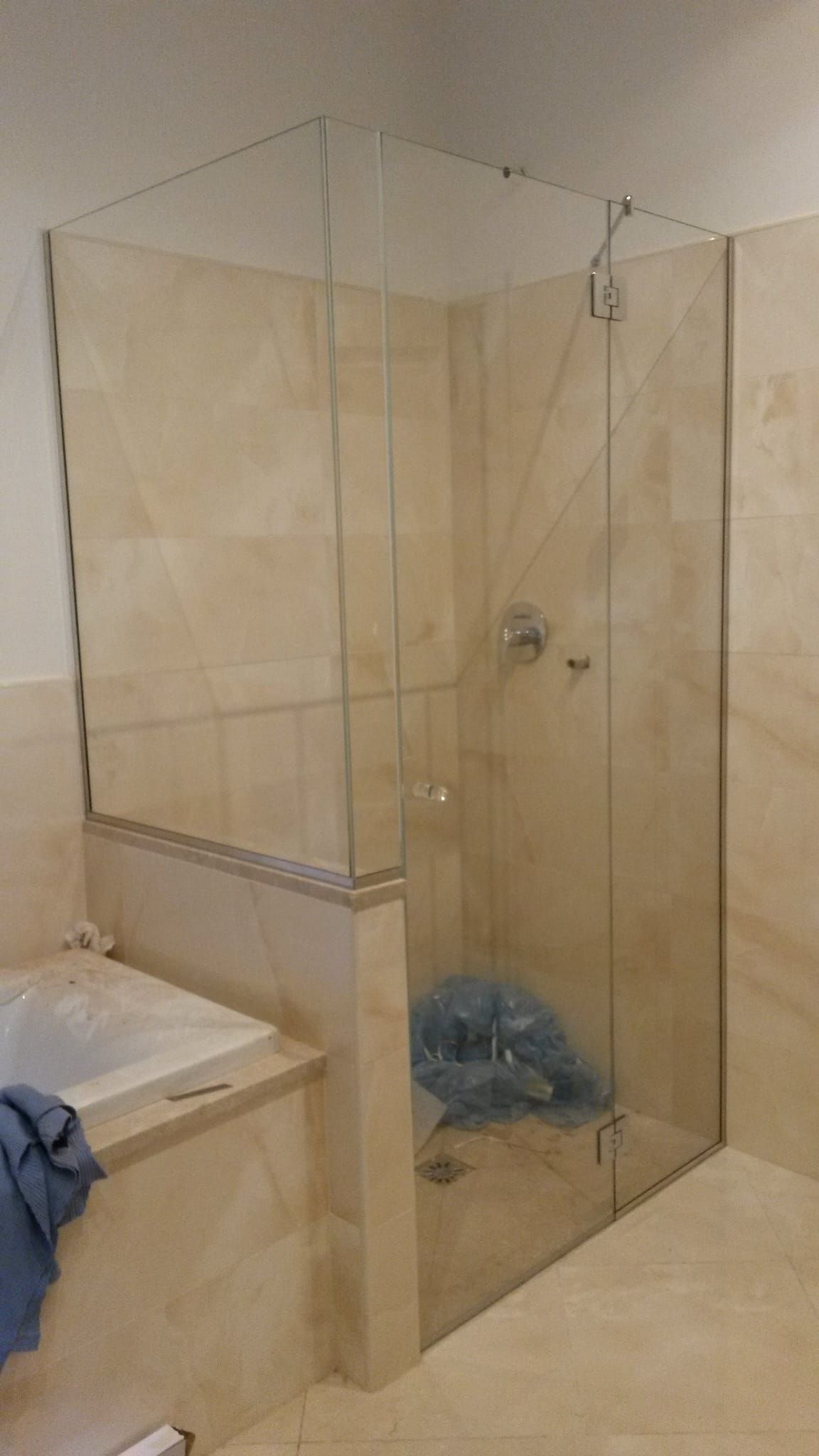 Bagno con box doccia in vetro, pareti rivestite con piastrelle beige e lavabo sulla sinistra.