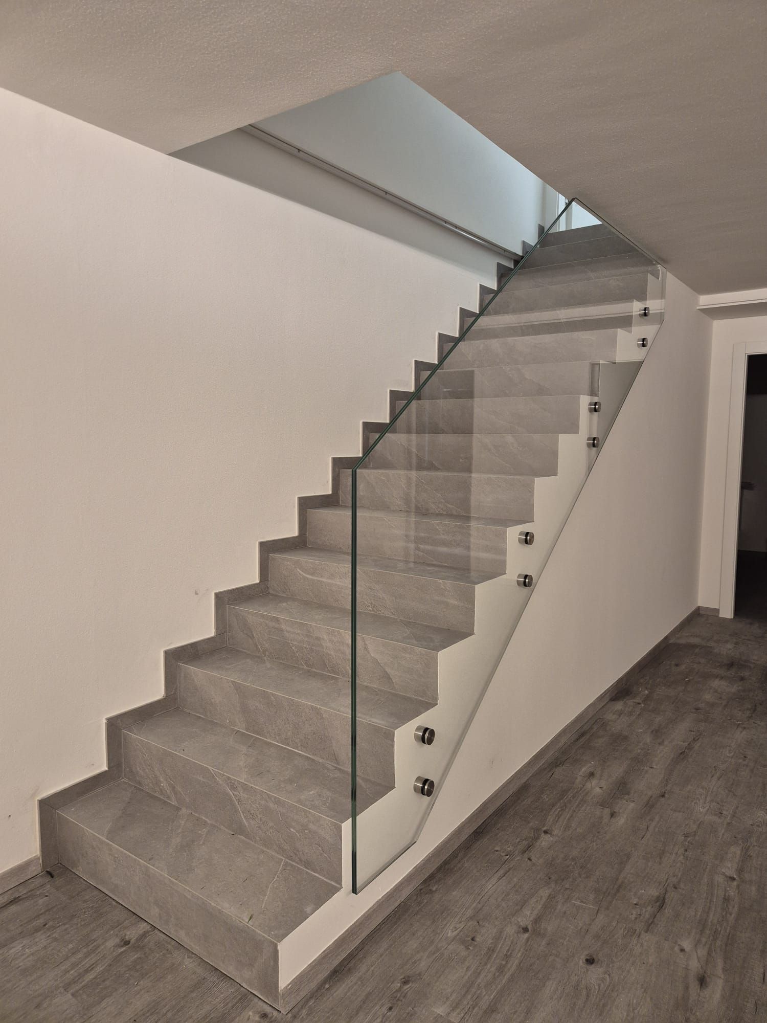 Scala interna moderna con gradini rivestiti in moquette grigia, ringhiera in vetro e pareti bianche.