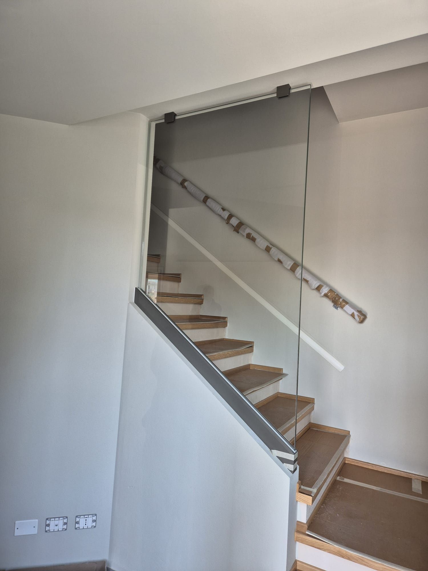 Scala interna con pareti bianche, gradini in legno, ringhiera in vetro e corrimano scuro sul pianerottolo.