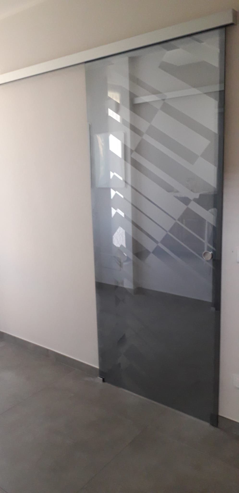 Porta scorrevole in vetro con strisce geometriche satinate in un corridoio interno semplice