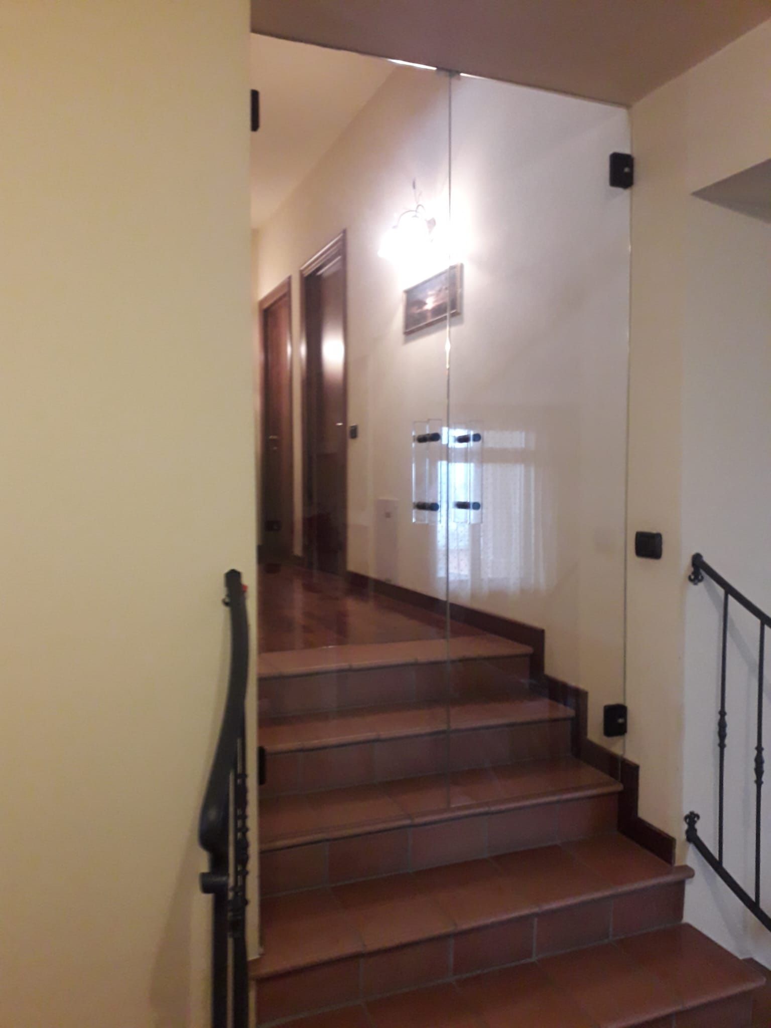 Vano scale interno con gradini piastrellati, corrimano scuri e pianerottolo in cima.
