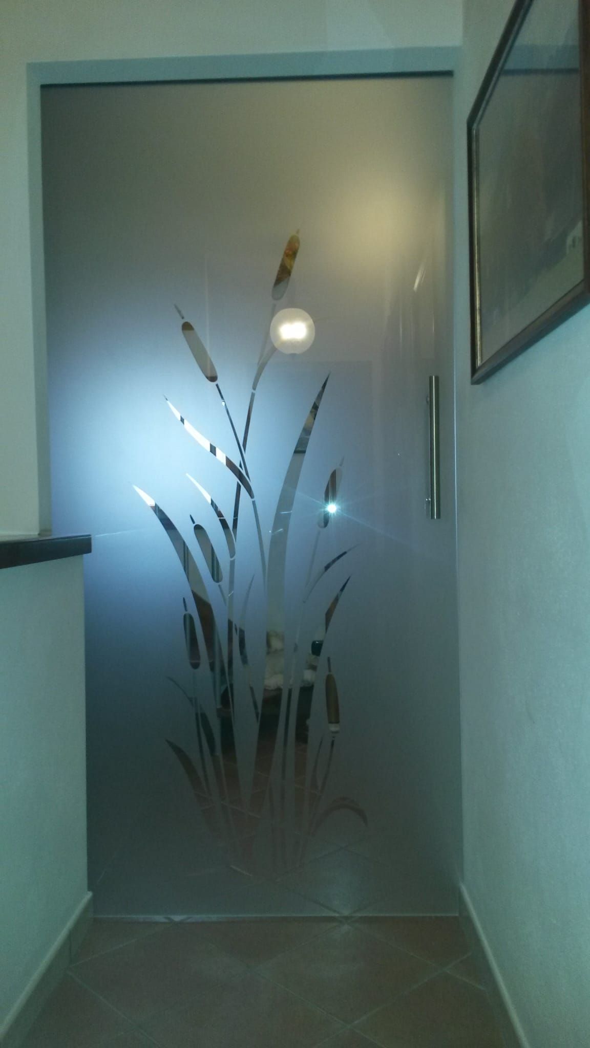 Porta in vetro satinato con canne incise e lampada rotonda, incastonata in un corridoio poco illuminato.