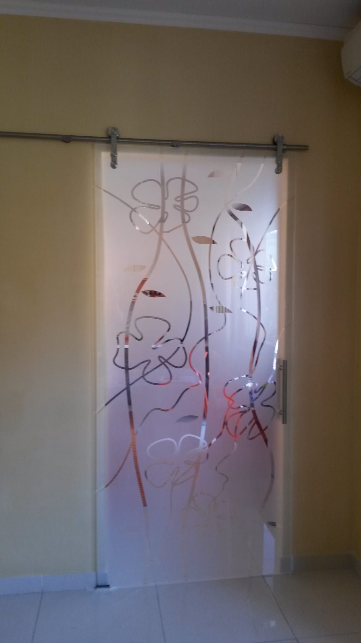 Porta astratta in vetro satinato con binario superiore argentato e motivi a vite rosso-marroni in un corridoio