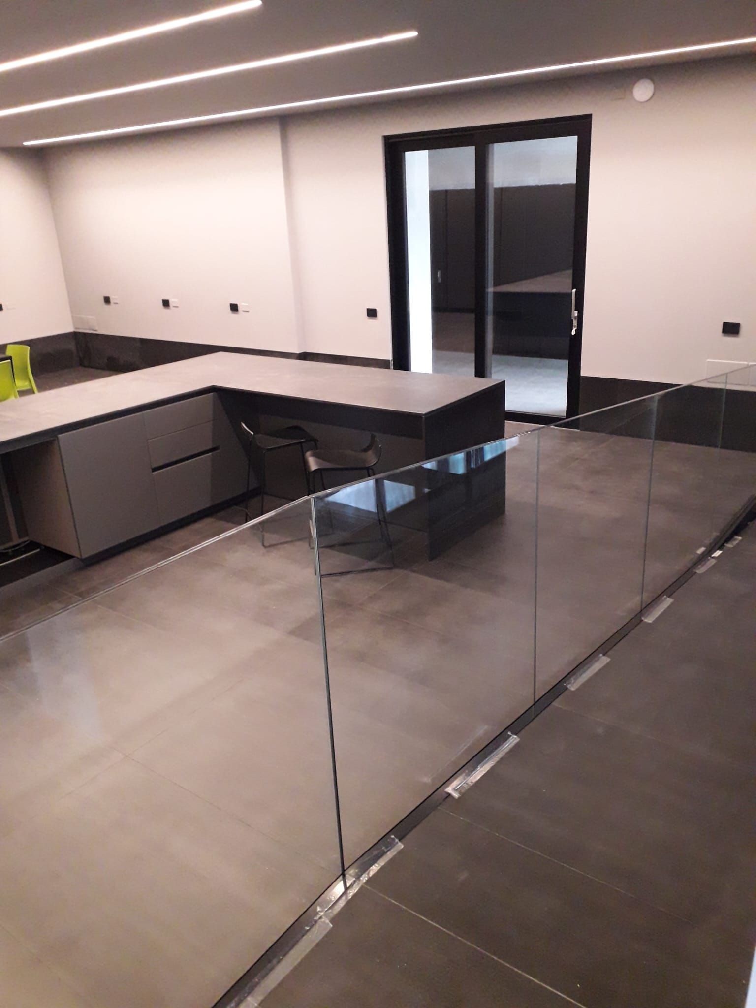 Cucina moderna e minimalista con mobili neri, isola in vetro e ampie finestre.