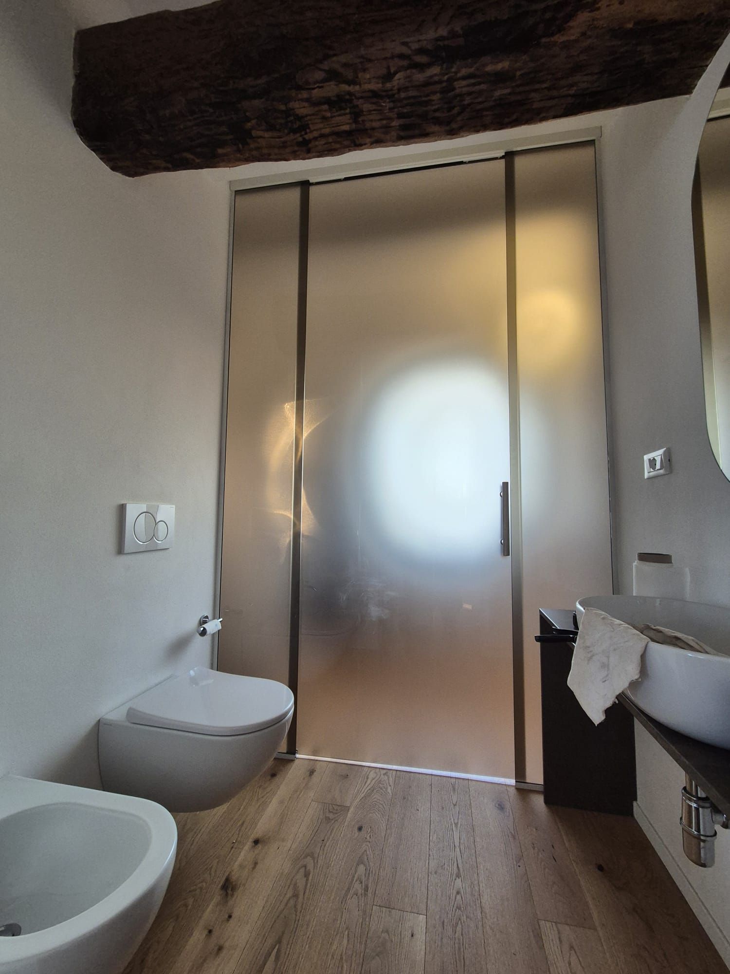 Bagno moderno con porte doccia in vetro satinato, lavabo a parete e pavimento in legno.
