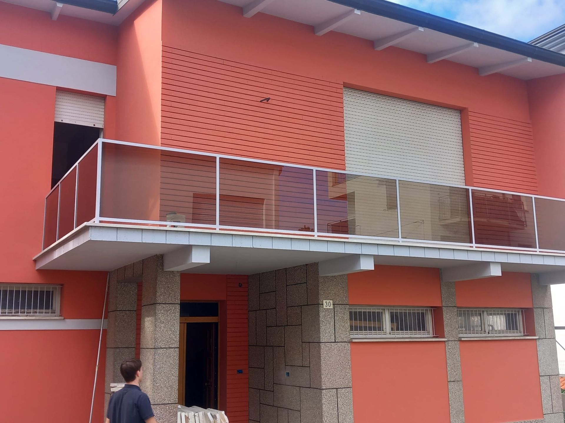 Persona in piedi davanti a un edificio color corallo con balcone e persiane arancioni