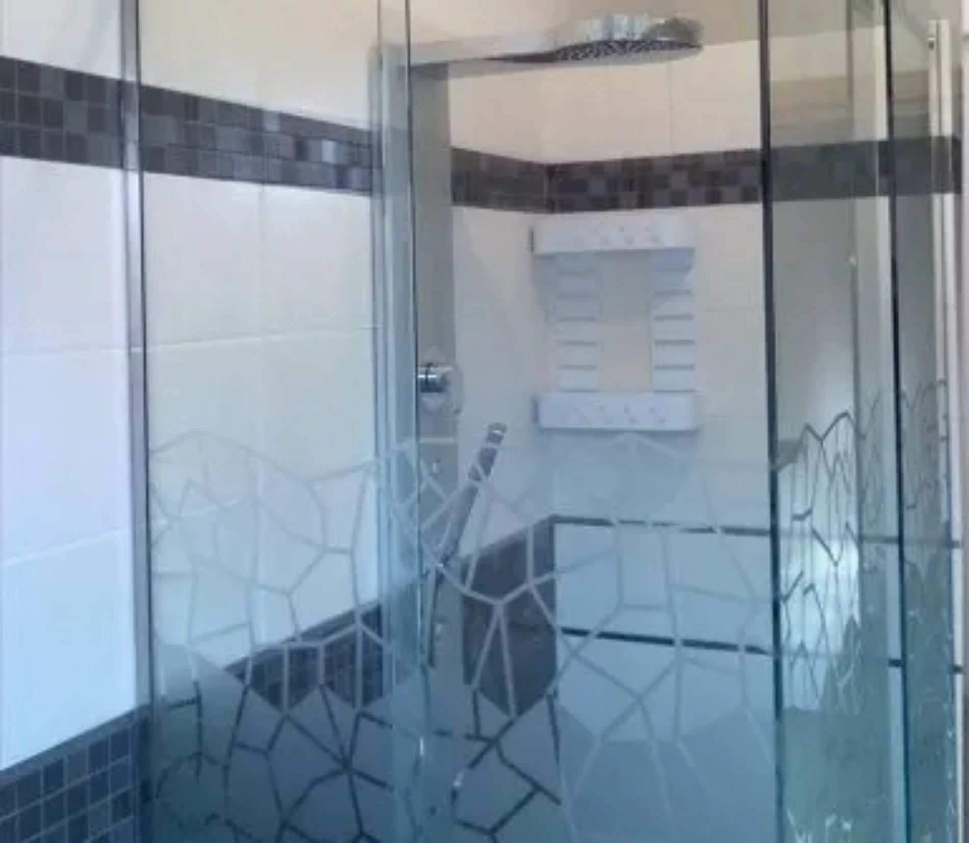 Box doccia moderno in vetro con motivo geometrico satinato, installato in un bagno piastrellato.