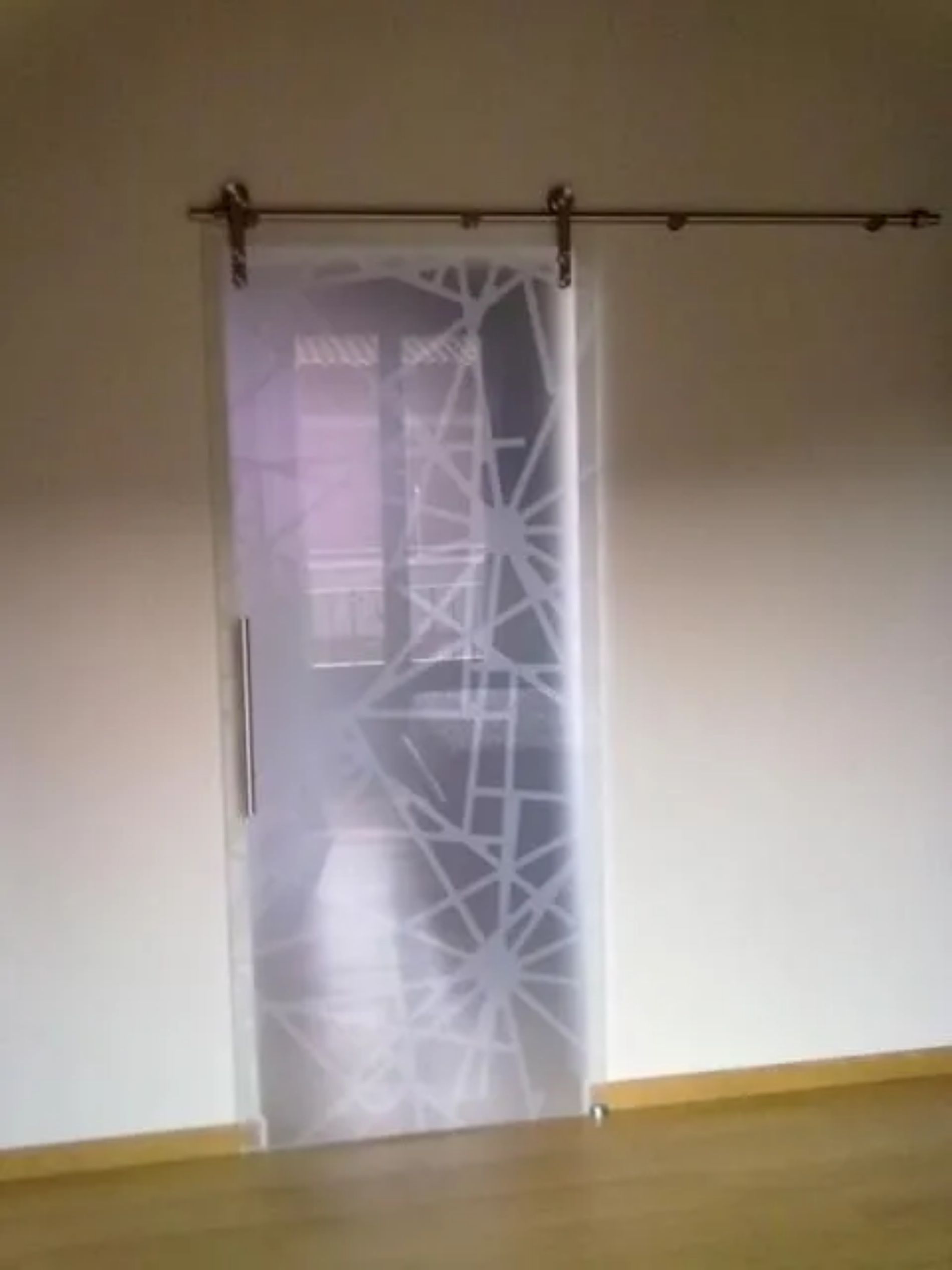 Una tenda trasparente a fantasia pende da un'asta sopra una porta in una stanza spoglia con pavimento in legno e pareti bianche.