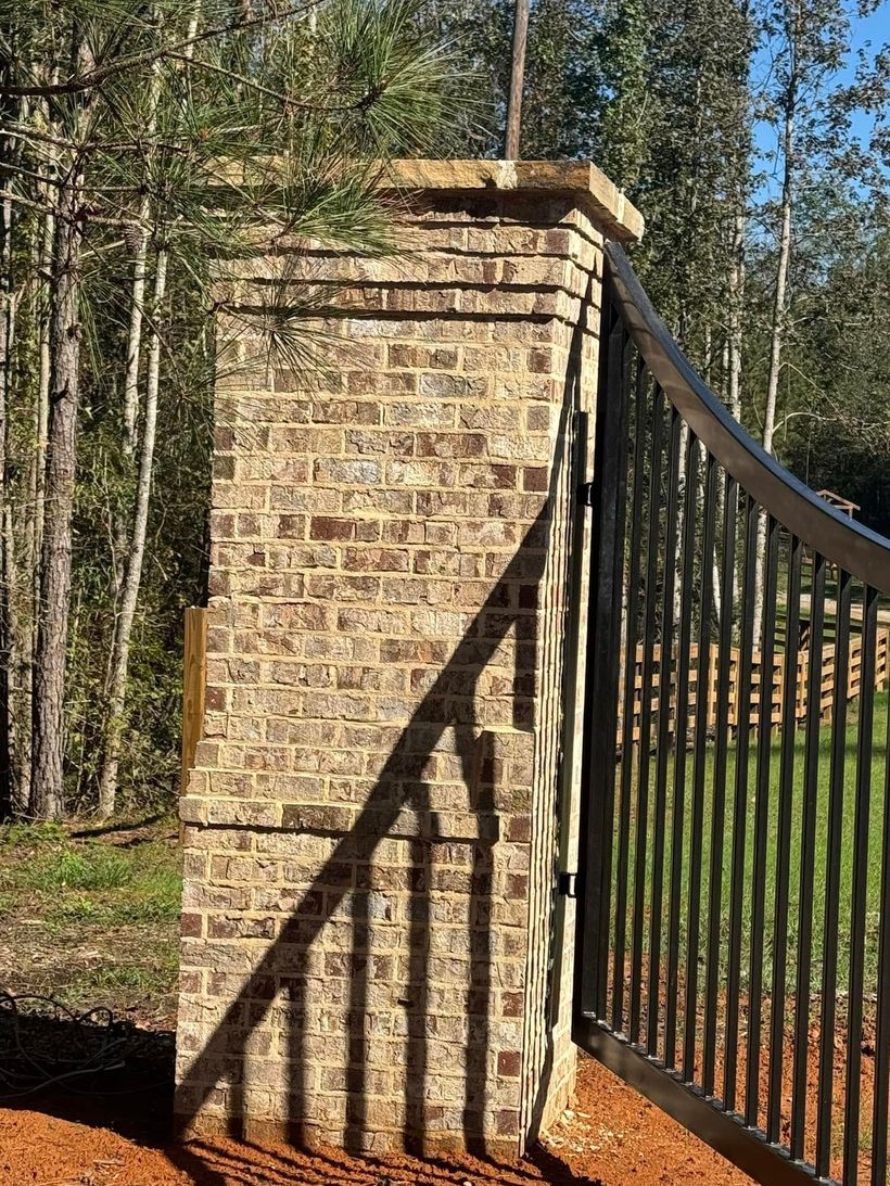 Brick pillar beside a black iron gate in a wooded outdoor setting