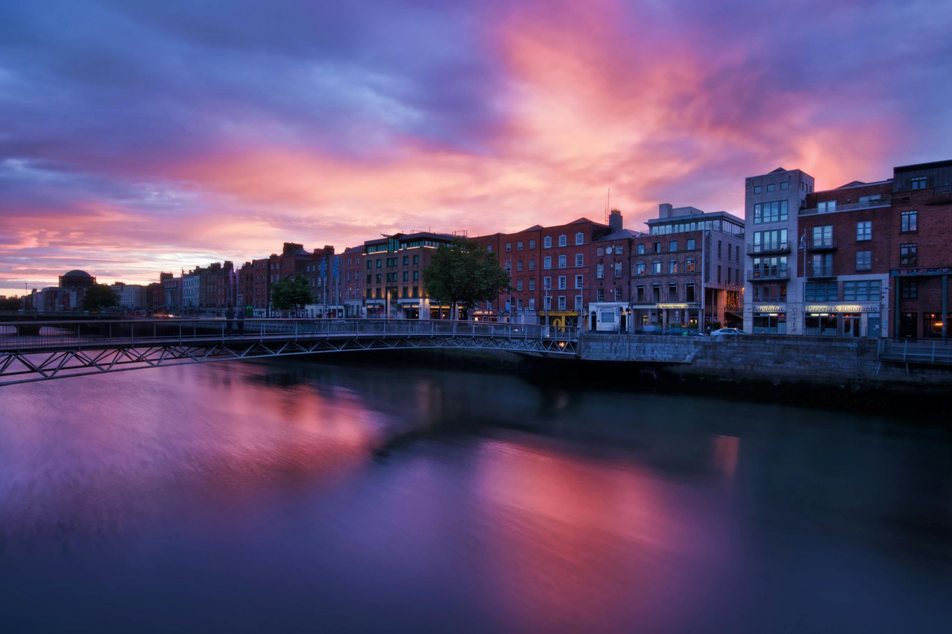 A bridge over a river with buildings in the background at sunset.
