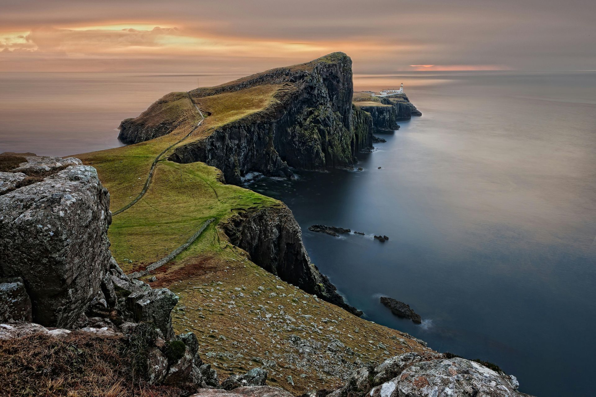 A cliff overlooking the ocean with a sunset in the background.