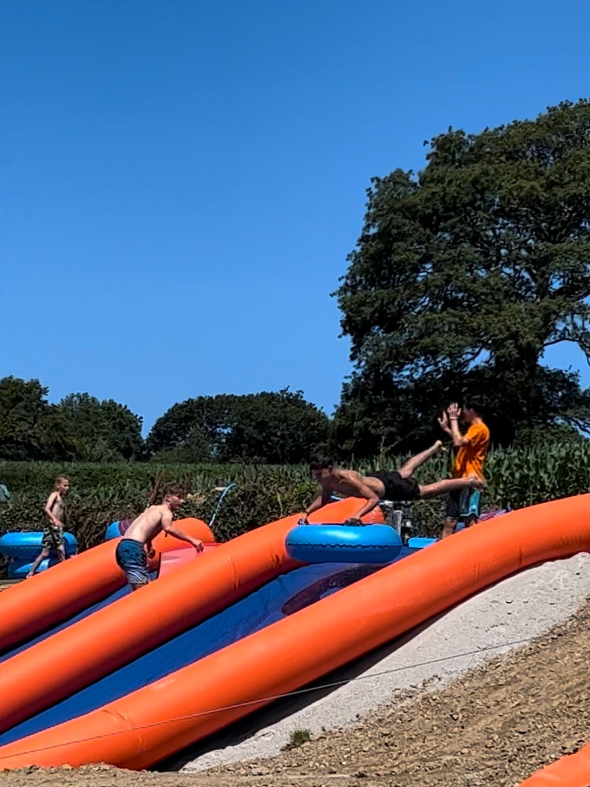 Three people on inflatable tubes slide down a large orange outdoor slide under a clear blue sky.